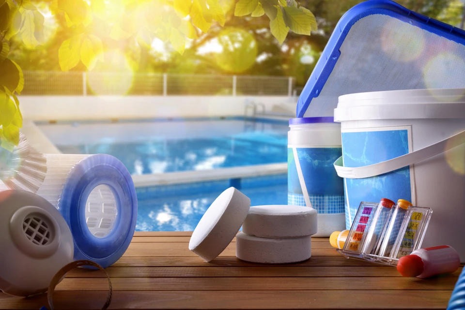 Scène extérieure ensoleillée au bord d'une piscine avec équipements d'entretien disposés sur terrasse en bois