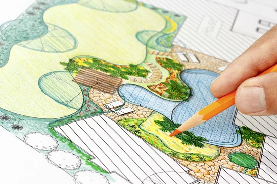 Une personne dessine à la main un plan d'aménagement paysager avec un crayon de couleur orange
