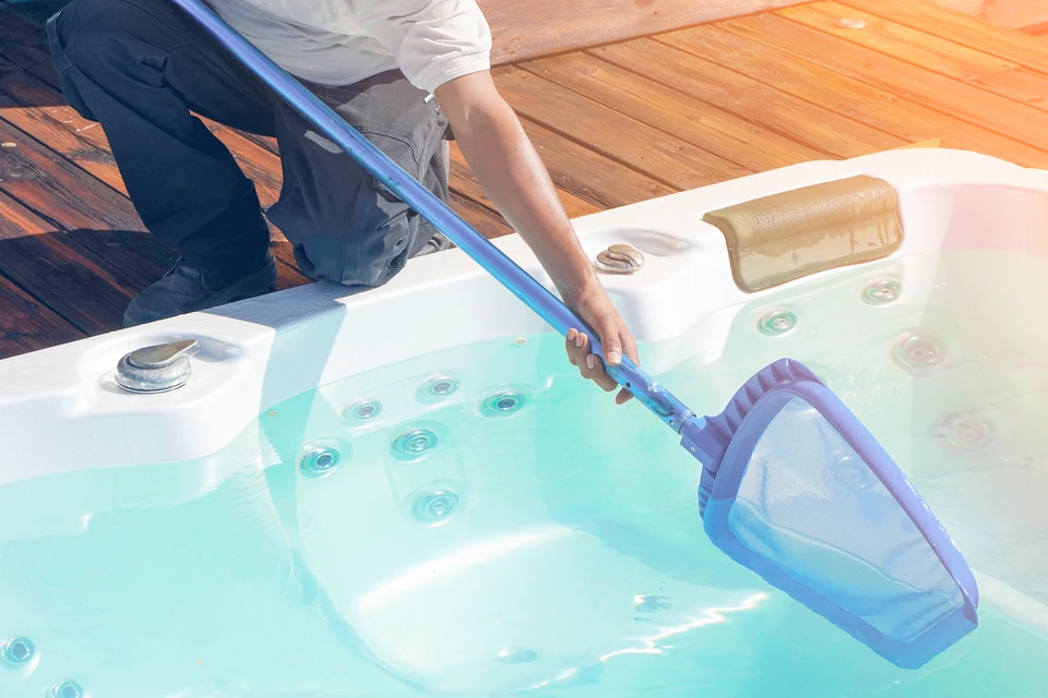 Scène extérieure sur terrasse en bois, personne nettoyant une piscine ou spa avec jets d'hydromassage actifs