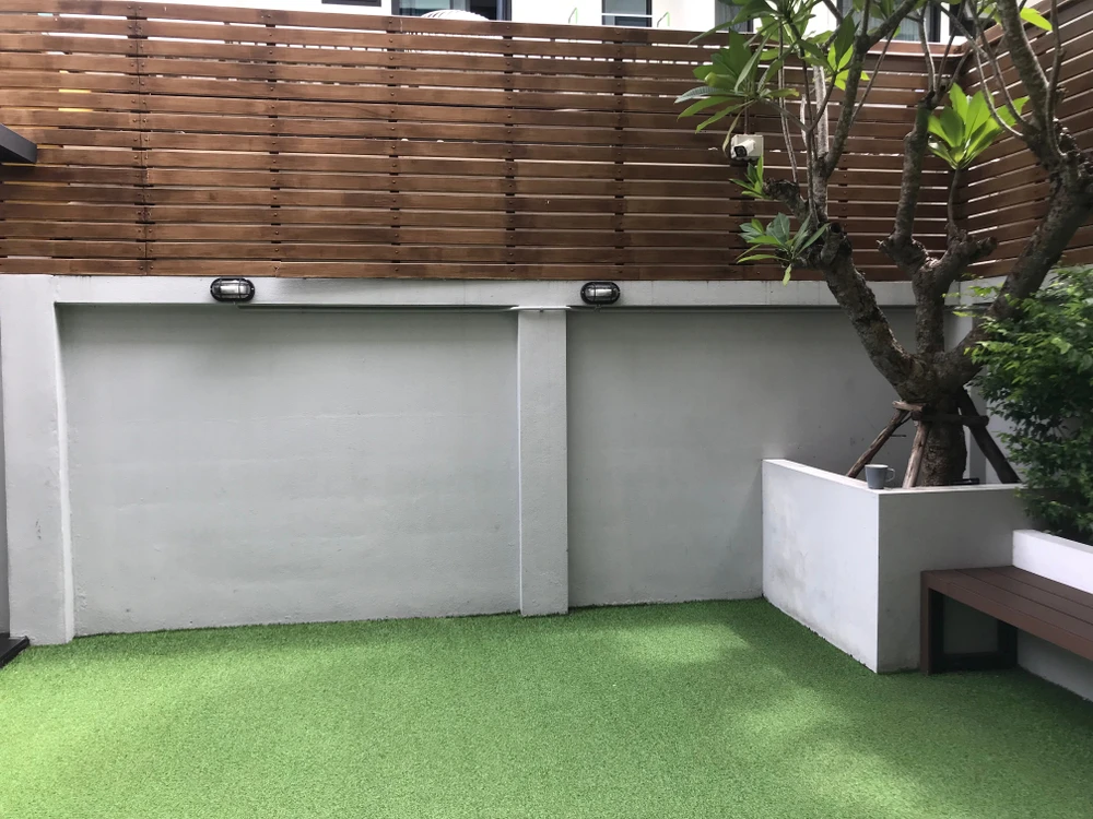 Espace extérieur moderne avec terrasse en gazon synthétique, murs en béton lissé gris clair, clôture bois à lames horizontales