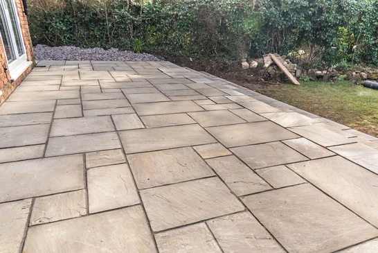 Terrasse extérieure en cours d'aménagement avec pose de dalles en pierre naturelle beige selon un motif géométrique irrégulier